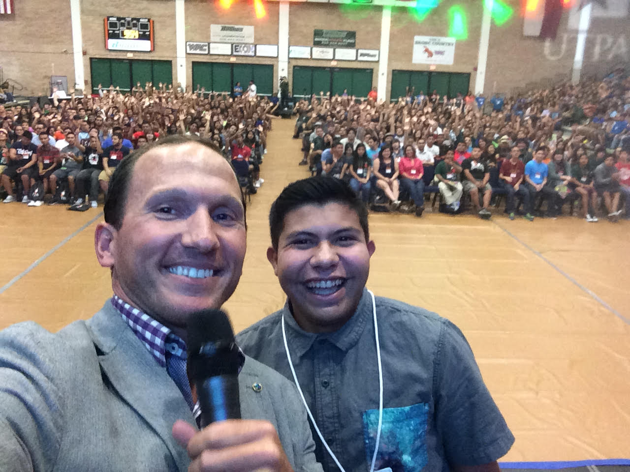 Kevin taking a selfie with a student in front of a packed gymnasium of youth